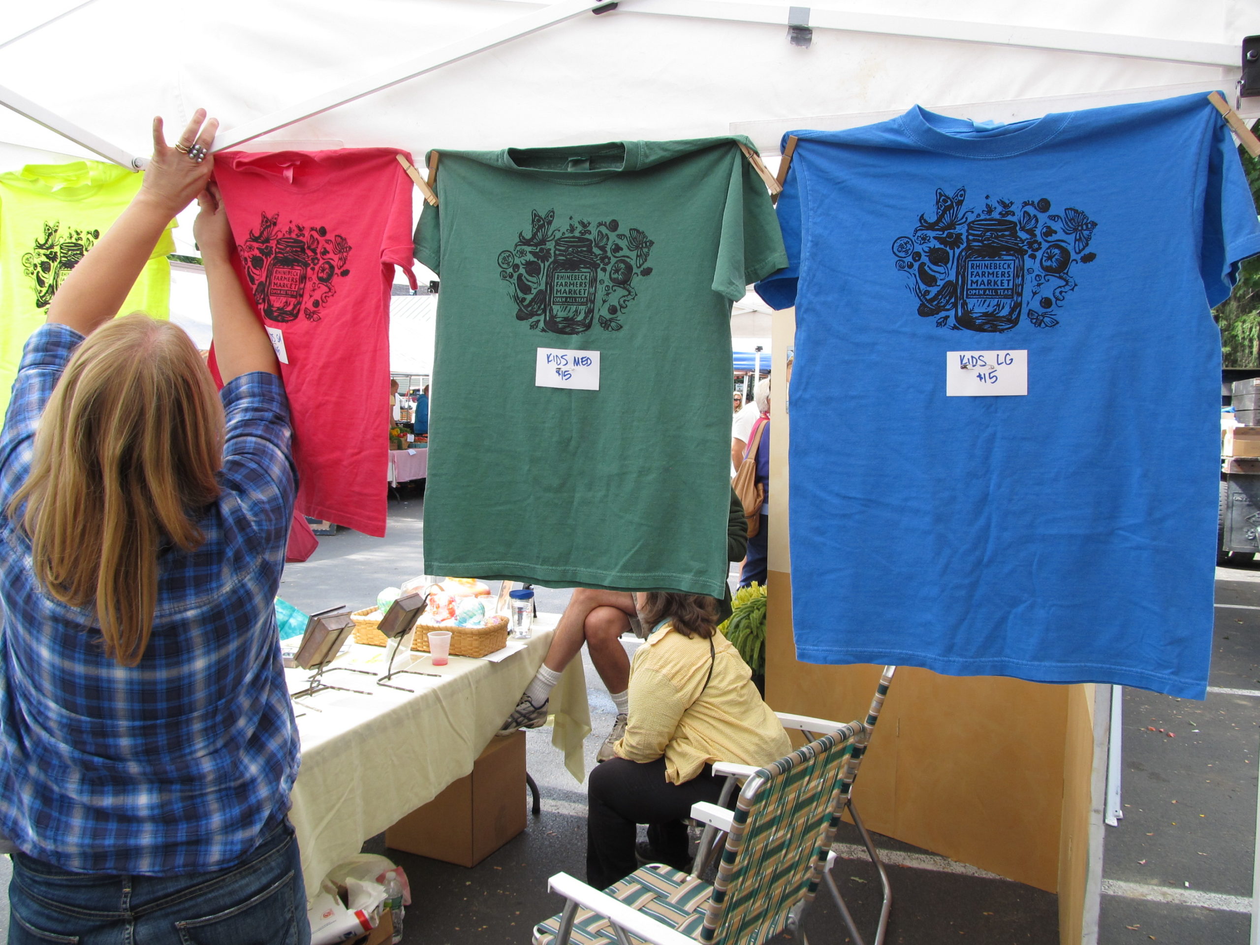 Cheryl Paff, Market Manager, sells brightly colored Market Tee-Shirts